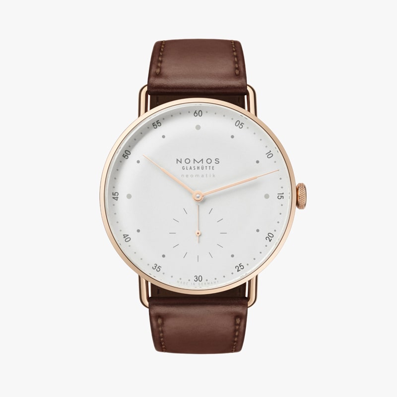 Eine minimalistische Armbanduhr, inspiriert von der NOMOS Metro, mit einem braunen Lederarmband und einem runden, weißen Zifferblatt. Sie verfügt über dünne goldene Stunden- und Minutenzeiger sowie schwarze Minutenmarkierungen. Das Design der Uhr ist schlicht und modern.