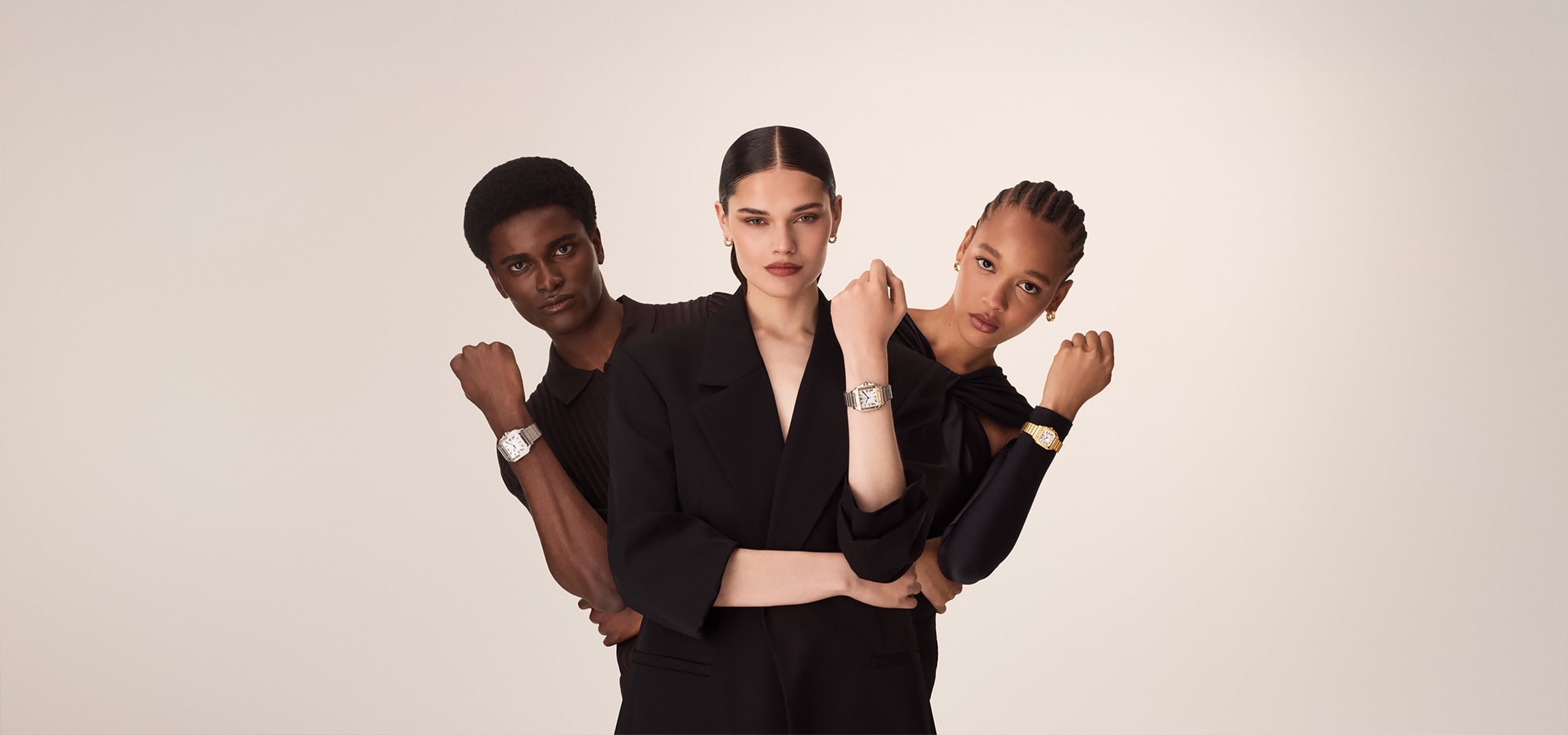 Drei Models in schwarzen Outfits stehen gemeinsam vor einem schlichten Hintergrund und präsentieren selbstbewusst die Armbanduhren der Santos Kollektion an ihren erhobenen Armen, während sie direkt in die Kamera schauen.